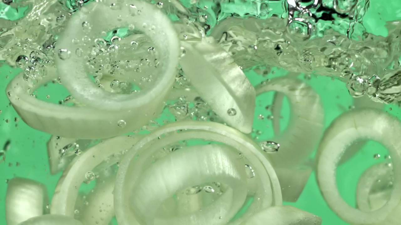 Friske hvide løgskiver flydende i vand med bobler.