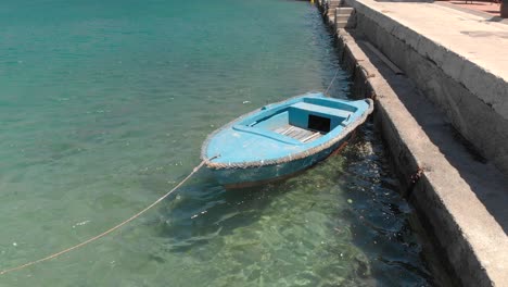 Ein-Einsames-Rustikales-Blaues-Hölzernes-Ruderboot-Schaukelt-Sanft-Im-Warmen-Klaren-Hafenwasser,-Kroatien,-Adriatisches-Meer