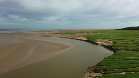 Aerial-shot-descending-over-a-coastal-bay,-on-a-bright-sunny-day,-natural-pattens-at-low-tide