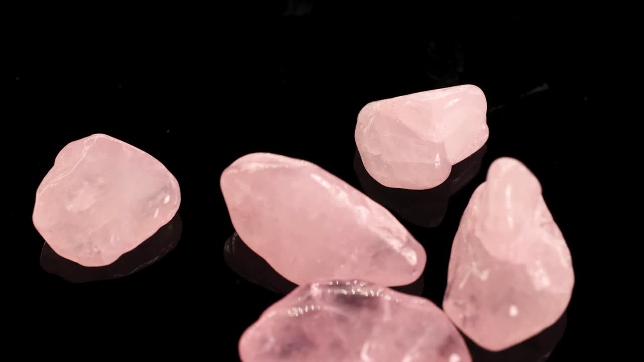 Rose quartz stones spin and fall gracefully on a reflective black surface, creating a serene and elegant visual effect