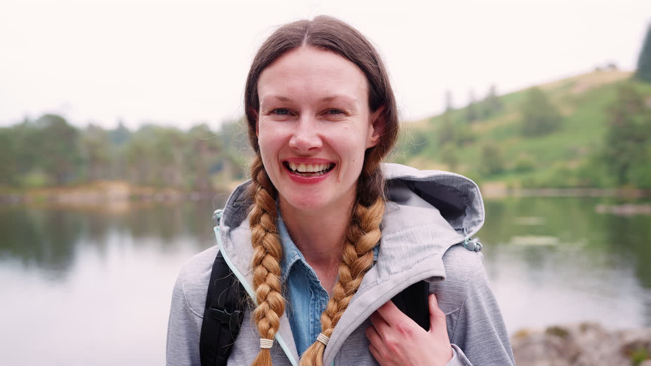 Young adult woman on a camping holiday standing by a lake laughing, close up, Lake District, UK