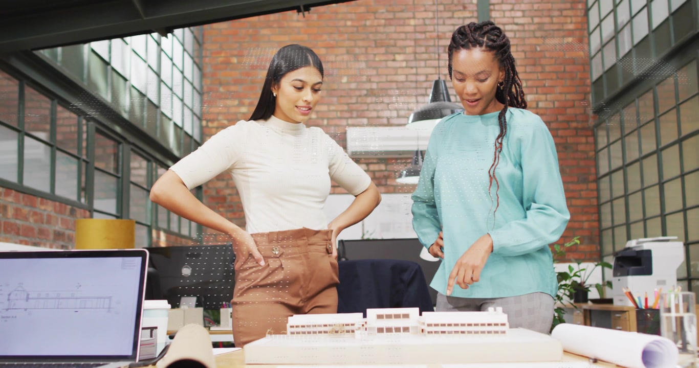 Right woman pointing, left woman leaning, reviewing scale model and plans for design decision