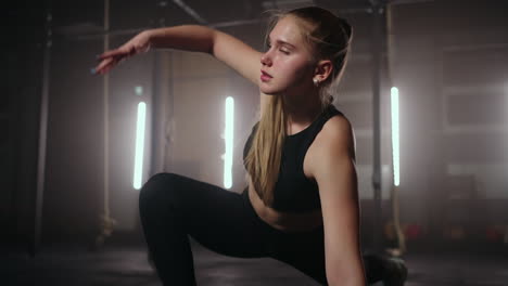 a young slender woman prepares and warms up before training. hitching and stretching muscles after a tedious hard workout in the dark interior of the fitness room