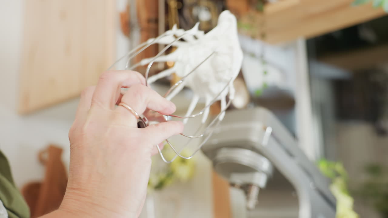 Chef removes electric mixer attachment covered with thick flour mixture and shakes it as batter clings to metal beater in home kitchen, showcasing baking process and texture of freshly whipped dough