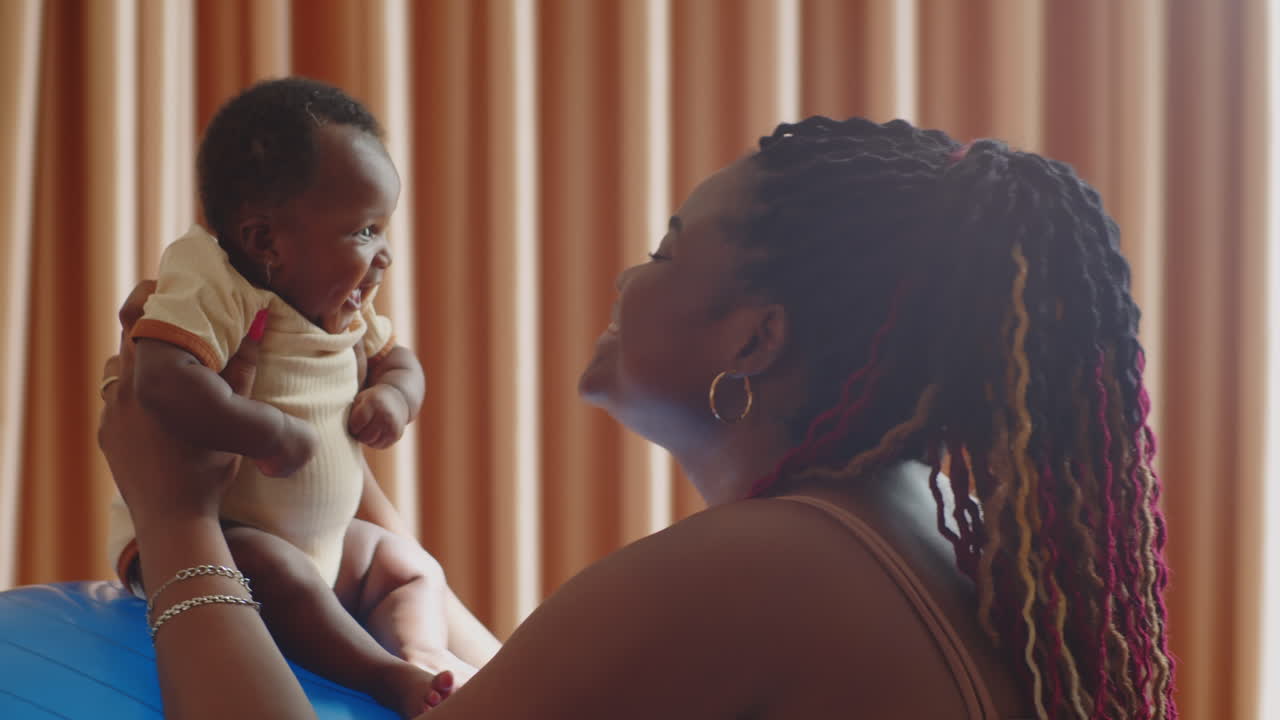 Mother Playing with Newborn Daughter Sitting on Fitball