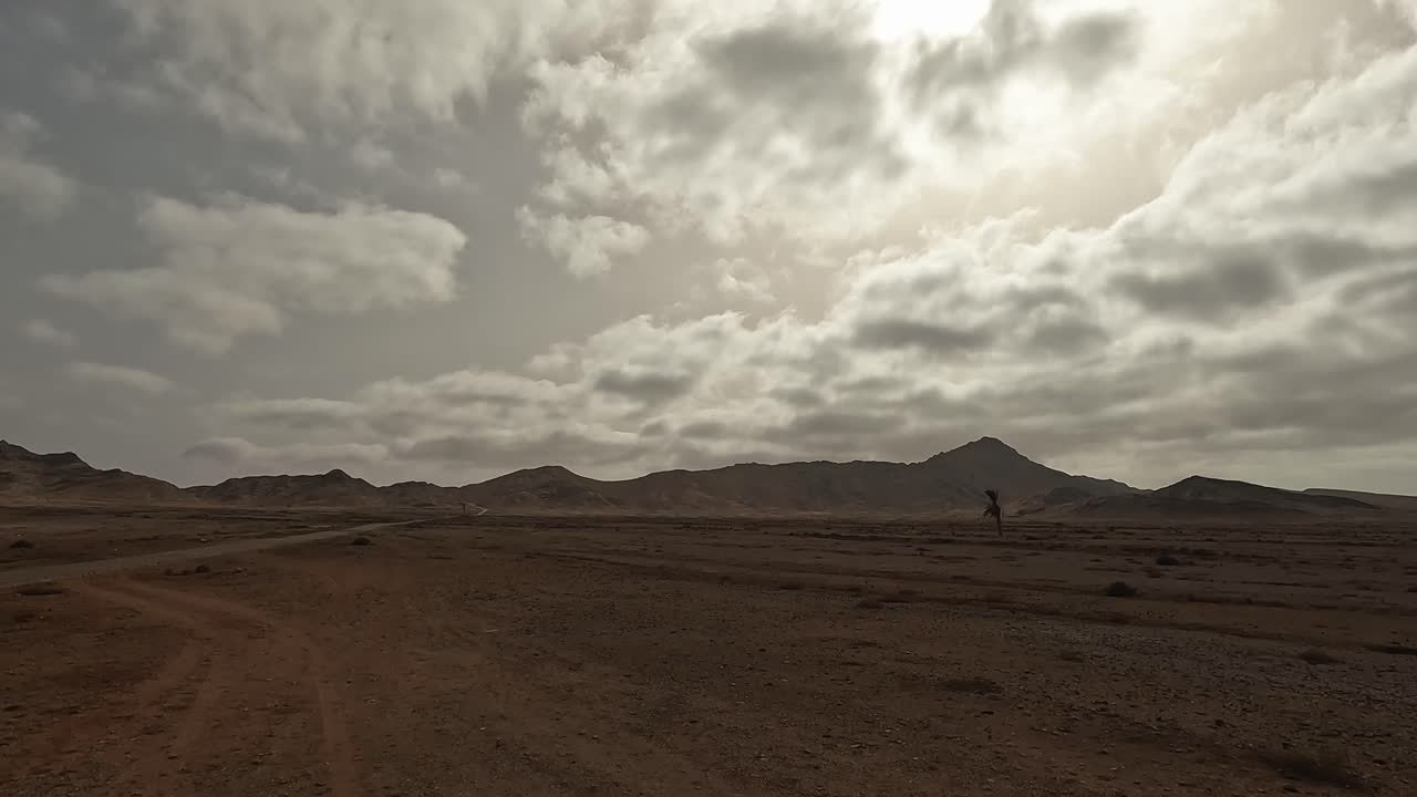 Panning view of arid landscape and dirt road of Boa Vista volcanic island with mountains in background. Cape Verde