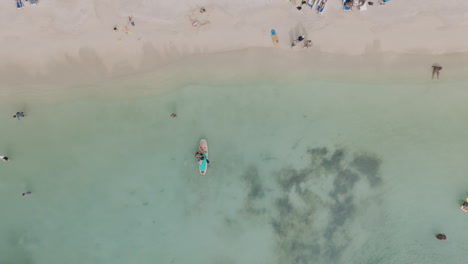 Aerial-cenital-dolly-Cinematic-View-of-A-Father-Teaches-His-Daughter-to-Stand-Up-Paddle-Enjoying-a-Sunny-Day-at-the-Beach,-with-Crystal-Clear-Turquoise-Sea-Featuring-Coral-Reefs-Ending-in-the-beach