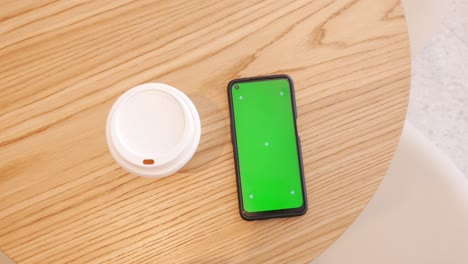 smartphone with green screen and coffee cup on a wooden table