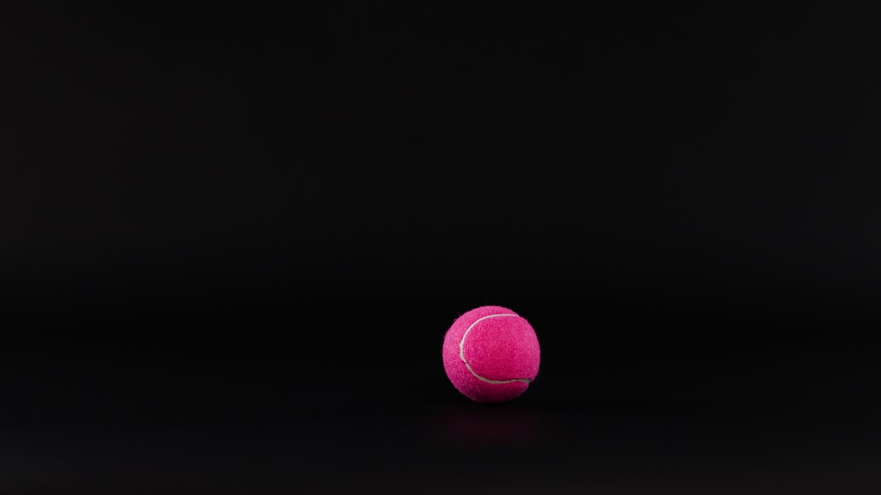 A pink tennis ball bouncing in darkness