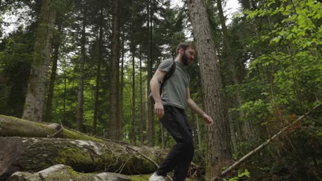 caucasian male jumps on tree logs in forest while on hiking adventure