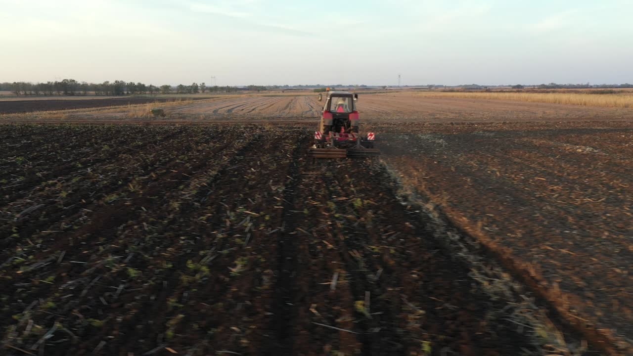 vista lateral aérea de un tractor que arrastra una harra de disco sobre un campo agrícola, tierras de cultivo