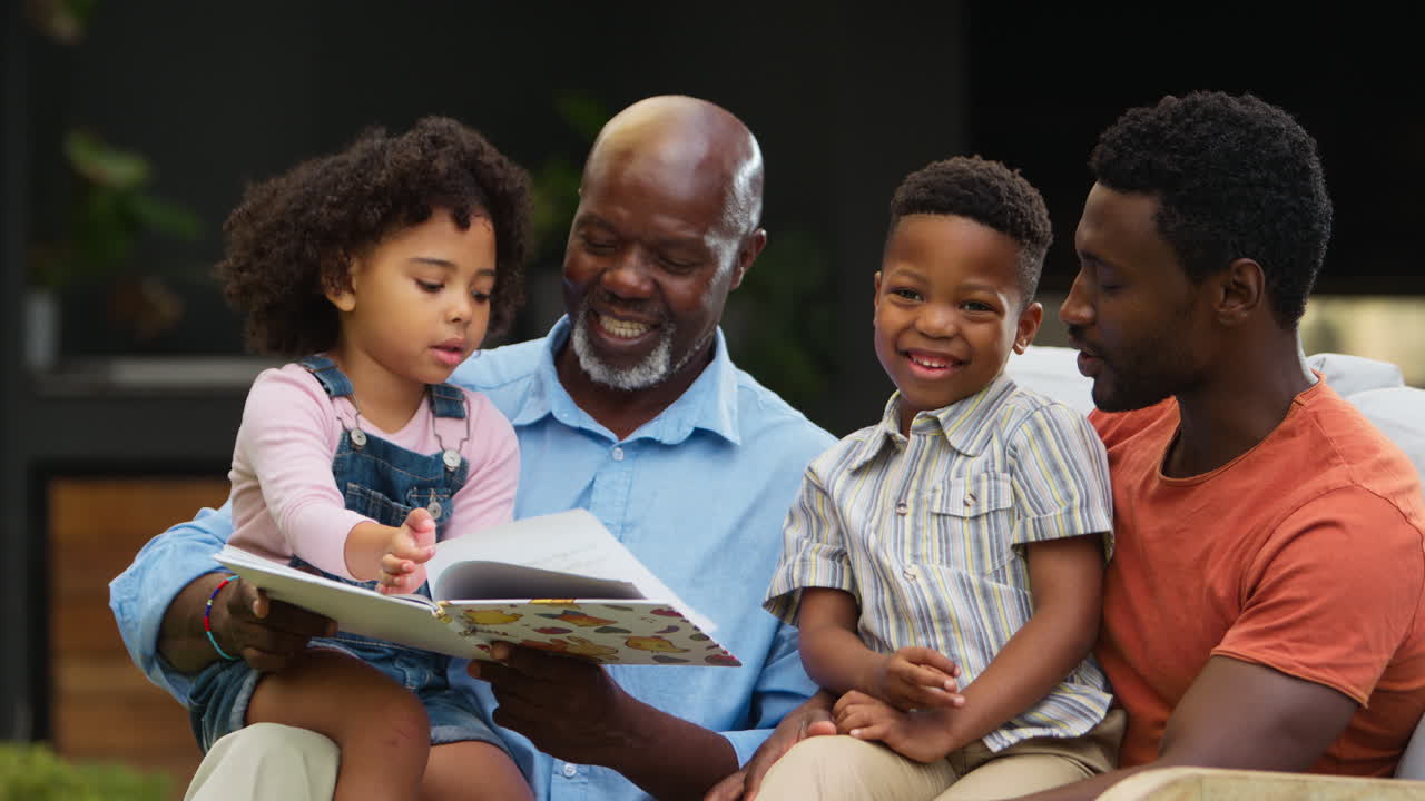 Smilende familie i flere generationer læser bog i haven sammen.