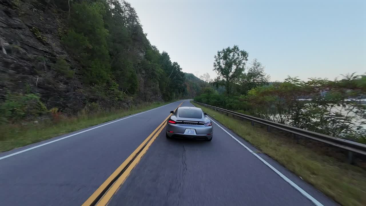 Aerial close following behind grey Sports Car nearby a river at sunset, US National Park