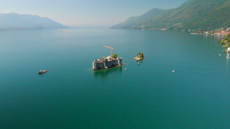 Aerial-approach-towards-a-small-island-with-a-ruin,-sorrounded-by-tiny-islands-in-the-middle-of-Lake-Maggiore,-Italy