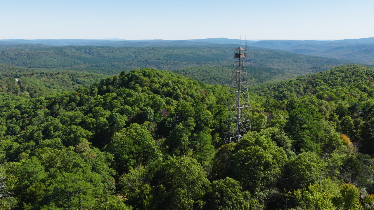 Vidvinkel flygbild bakåt av skogsklädda kullar och avlägsna åsar nära Devils Knob Lookout i Arkansas, torn på höger sida en tredjedel in