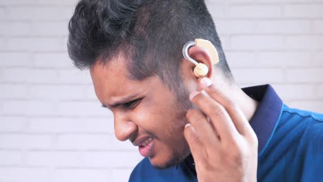 man with hearing aid touching ear in pain