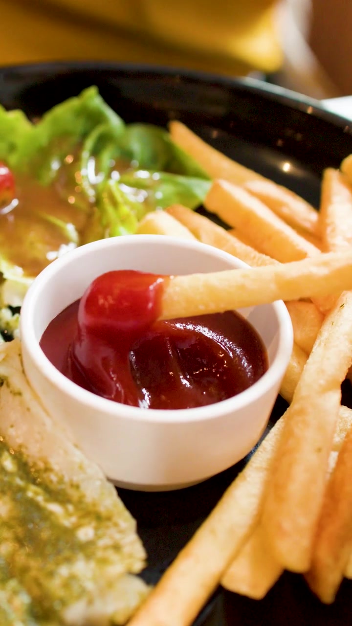 Primo piano di una mano che intinge una patatina fritta dorata nella salsa ketchup di pomodoro rossa.