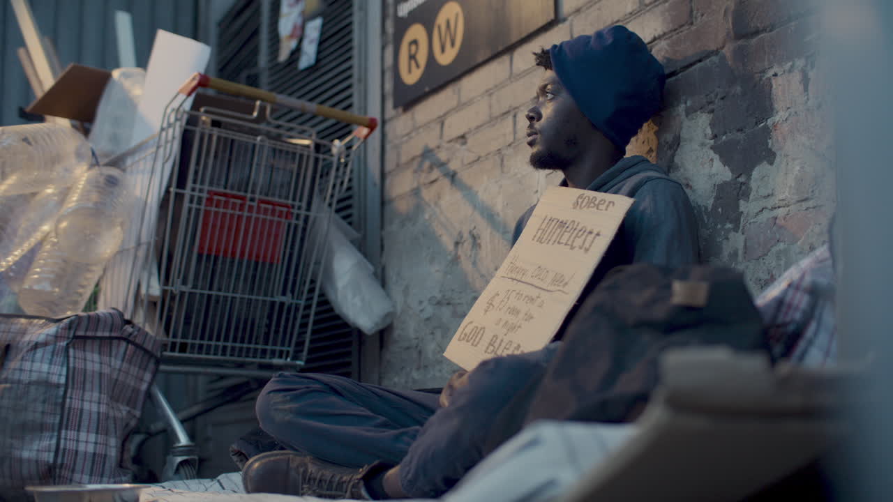 Homeless Man Sitting in Urban Alleyway, Holding Sign Asking for Donations