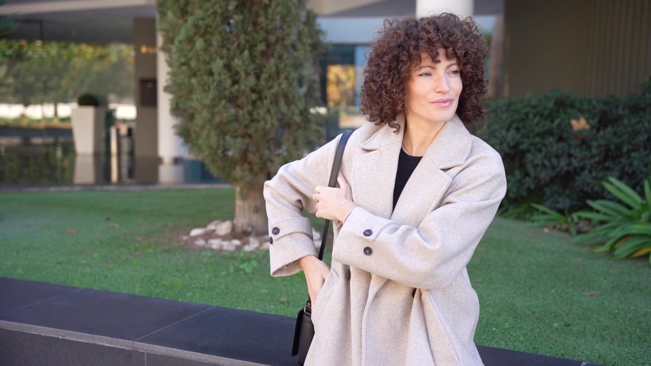 Una donna elegante con bellissimi capelli ricci in posa in un moderno ambiente esterno sotto la luce naturale