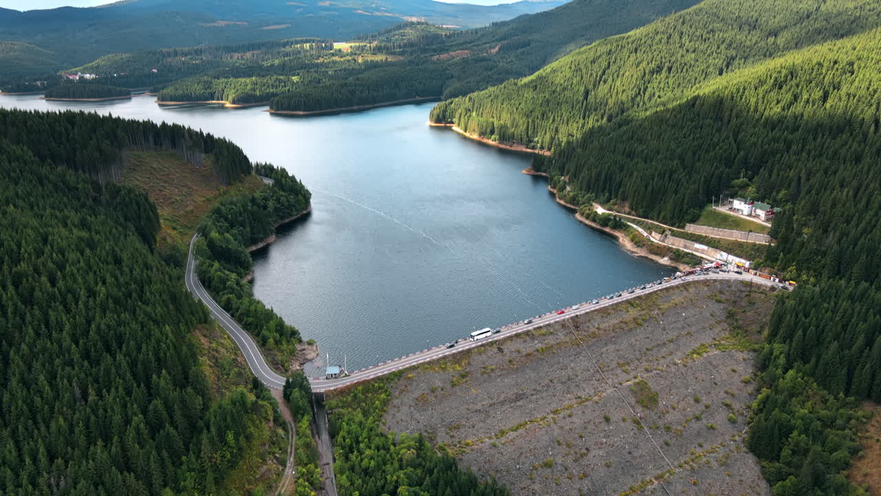 Aerial drone view of the Oasa Dam in Romania. Carpathian mountains, hills with lush forest, multiple cars