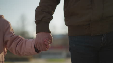 front view of a little girl wearing a pink jacket holding hands with a faceless man in a brown jacket and blue jeans. the scene captures a moment of connection and warmth on a sunny day