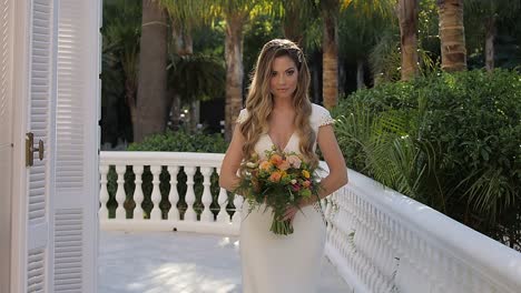 blonde bride with bouquet and wedding dress walking on sunny balcony garden