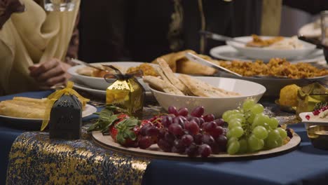 close up of muslim family sitting around table with food for meal celebrating eid being served