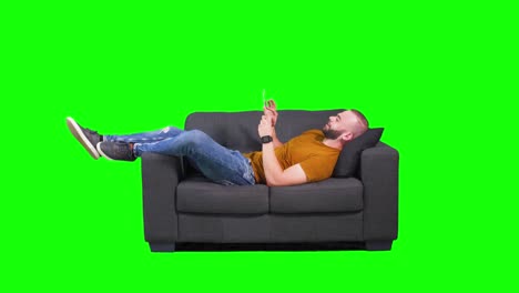 young hipster man using tablet while lying down on sofa