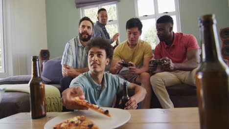 happy diverse male friends watching tv and drinking beer in living room