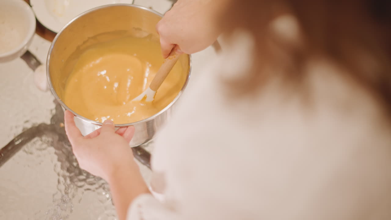 Overhead smoothing pumpkin filling into pan, soft back view of baker in white blouse, scattered plates and utensils, warm sunlight highlights glossy surface, circular strokes perfecting texture