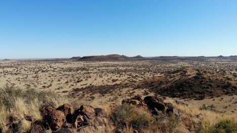 A-wide-shot-moving-from-the-top-of-a-hill-reveals-a-large-African-savanna-under-a-bright-blue-sky