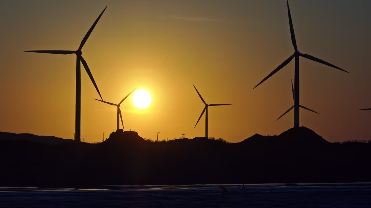 tomada de un dron de lente larga de siluetas de turbinas eólicas y kitesurfistas durante la puesta de sol en brasil