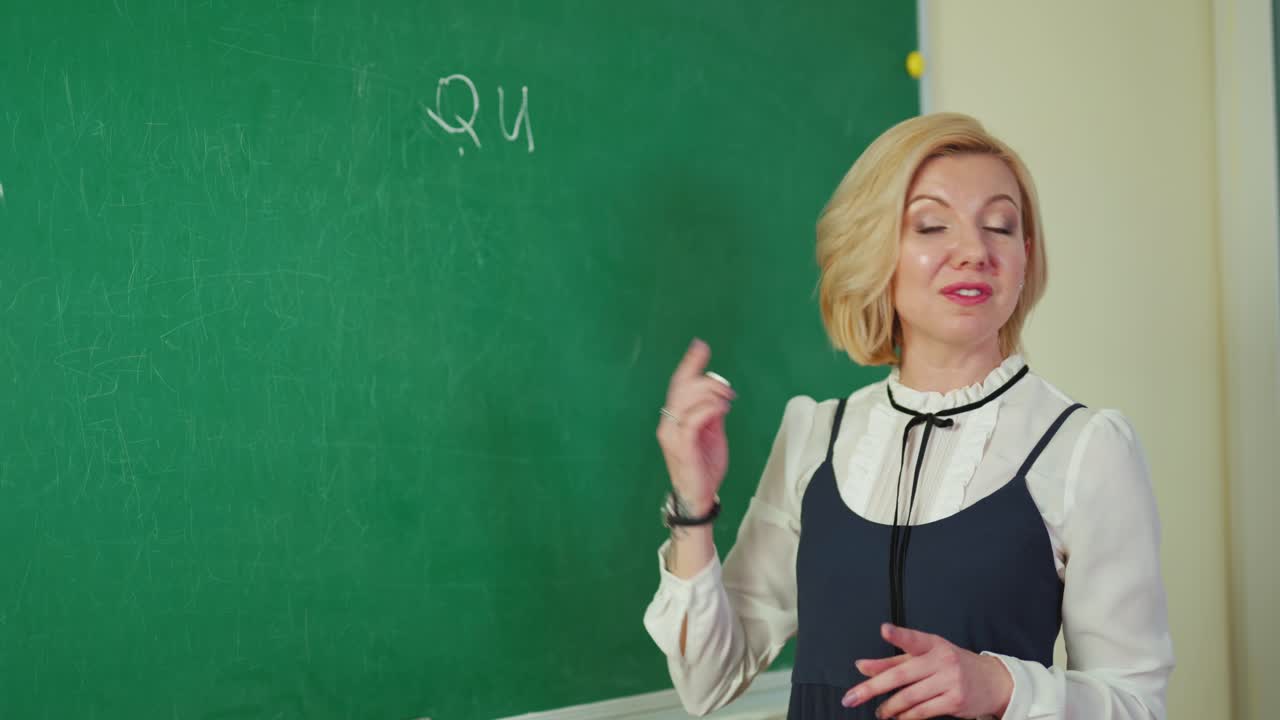 Education concept. Beautiful teacher writes on a blackboard. Creative female teacher standing near the chalkboard and writing with white chalk.