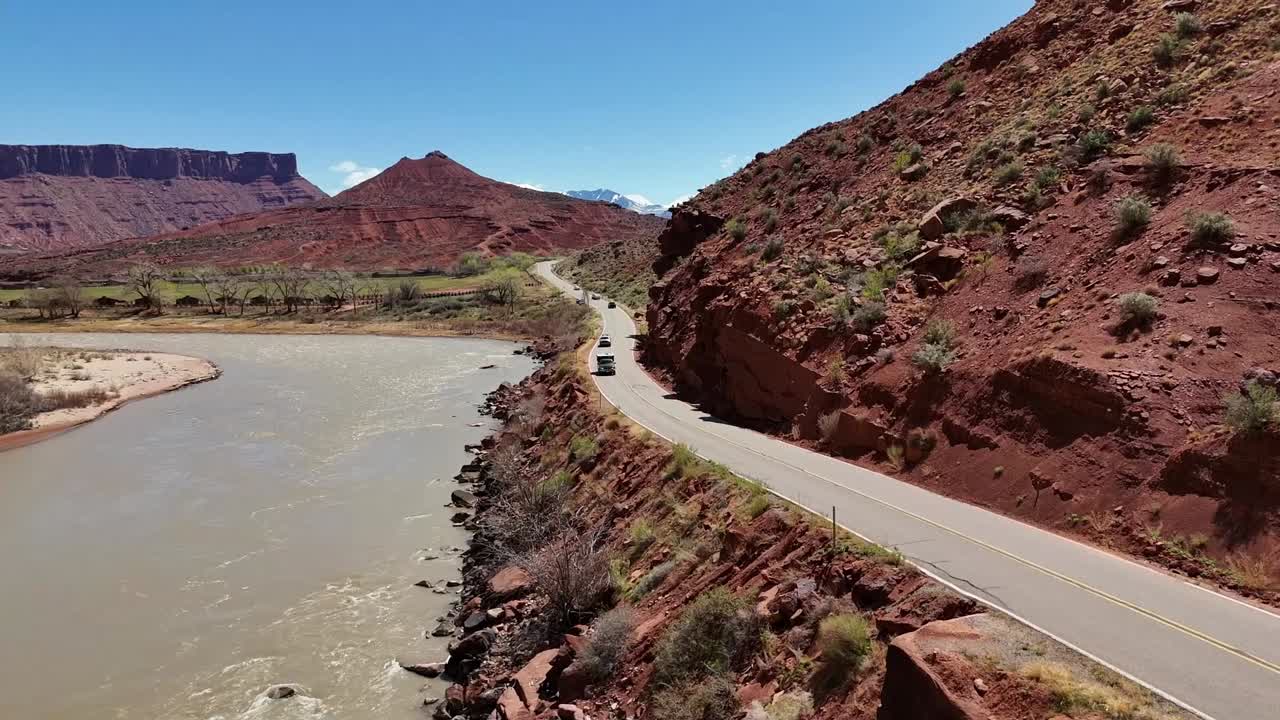 Cars Driving down Road next to River, Highway 128 in Moab Utah, Colorado River, Mountains in background.