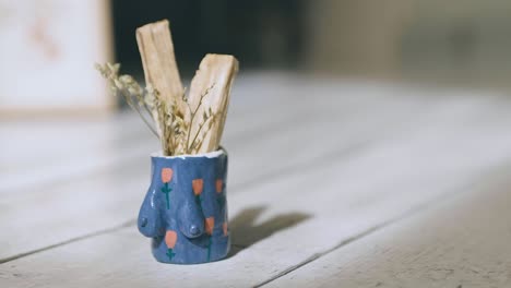 Small-feminist-vase-with-little-flowers-painted-on-it,-inside-holy-pole-and-twigs