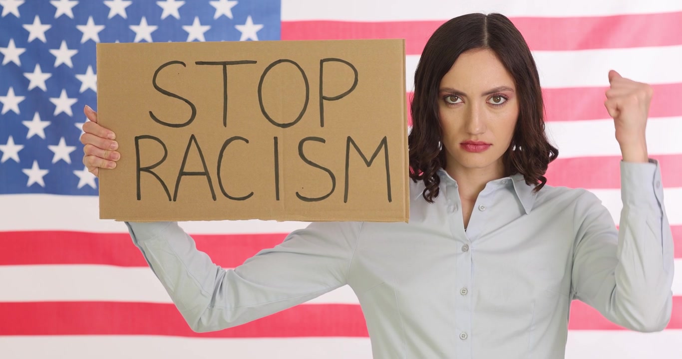 Una donna mostra un cartello "stop al razzismo" agitando il pugno contro la bandiera americana
