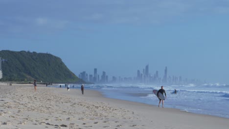 people enjoying palm beach - surfers riding waves - surfers paradise on the background - gold coast, queensland, australia