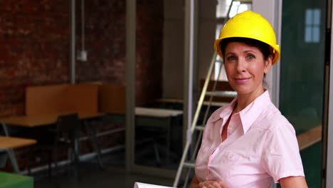 Focused-architect-holding-blueprints-and-smiling-at-camera