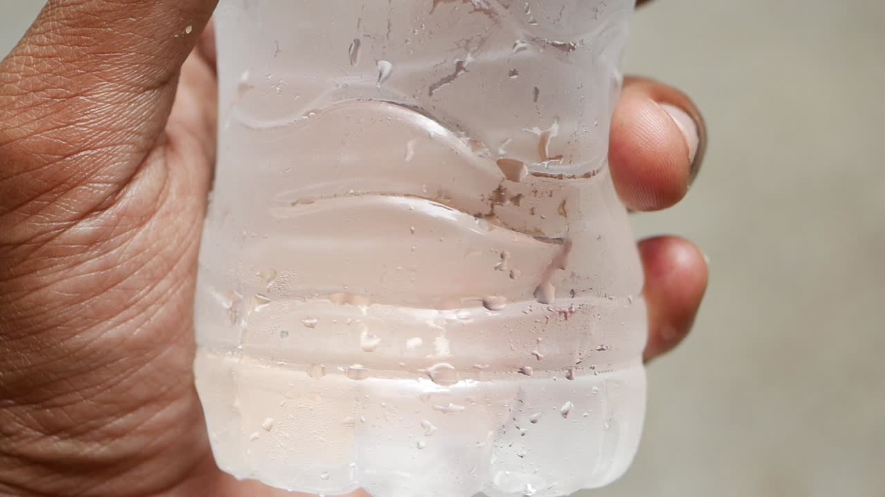 primer plano de una mano sosteniendo una botella de agua fría