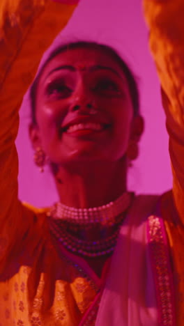 vertical video close up on face of female kathak dancer performing dance wearing traditional indian dress against purple background