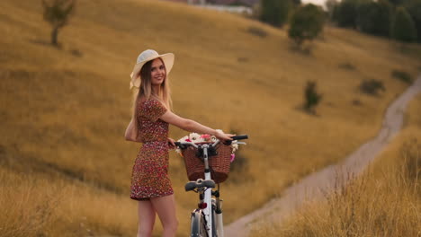 Lens-flare:-smiling-happy-woman-in-short-dress-is-riding-a-bicycle-with-a-basket-and-flowers-in-the-park-with-green-trees-around-during-the-dawn.-Slowmotion-shot