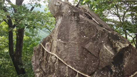 Japanese-stone-shrine-offerings-with-coins-for-prayer-in-a-green-mountain-forest