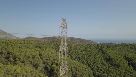 Toma-Aérea-De-Carro-Hacia-Atrás-De-Un-Poste-De-Transmisión-De-Alto-Voltaje-En-Las-Montañas