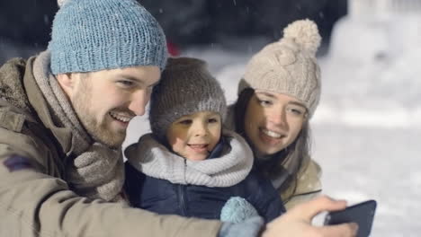 couple with their son in winter clothes making a video call in the park while it snows