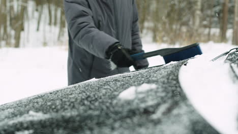 冬の日にブラシで雪から車を掃除する認識できない男のクローズアップ