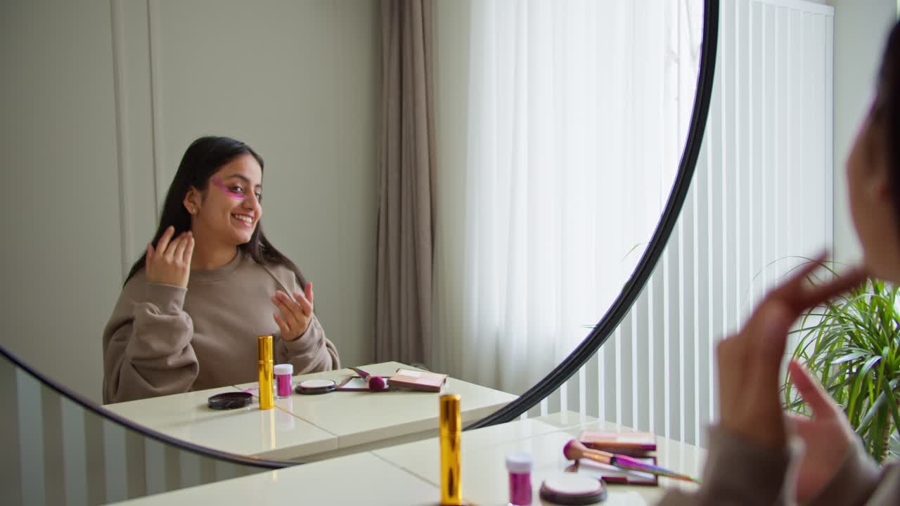 A brunette girl in a brown sweater applies special cosmetic patches to her face under her eyes to moisturize the skin and give it a natural color while doing makeup and looking at her skin in a modern apartment during the day
