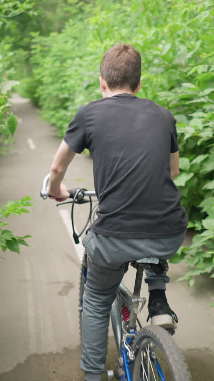 색 도로 표시가 눈에 띄는 울창한 초록색으로 둘러싸인 경치 좋은 포장된 길을 따라 자전거를 타고 있는 사람의 뒷면, 빛은 자전거 타는 사람이 앞으로 페달을 는 동안 반사됩니다.