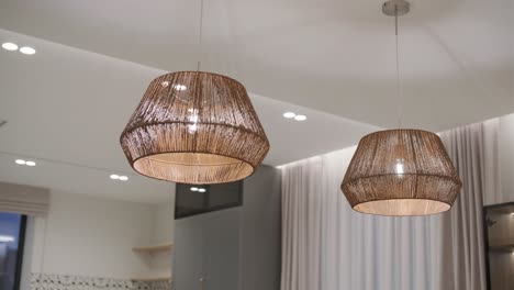 dos luces colgantes tejidas cuelgan con gracia, proyectando una iluminación cálida y texturizada sobre una habitación contemporánea, mezclando elementos naturales con diseño moderno