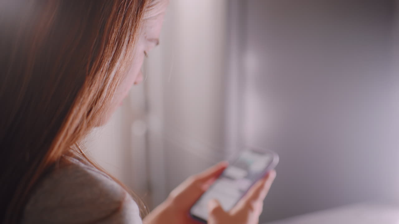 Close up of woman holding smartphone while scrolling through chat messages, focused expression visible as soft daylight highlights face and hair, reflecting digital lifestyle and everyday communication