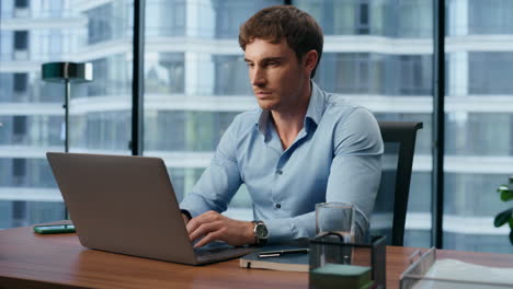 Pensive-businessman-typing-keyboard-at-panoramic-workplace.-Manager-working